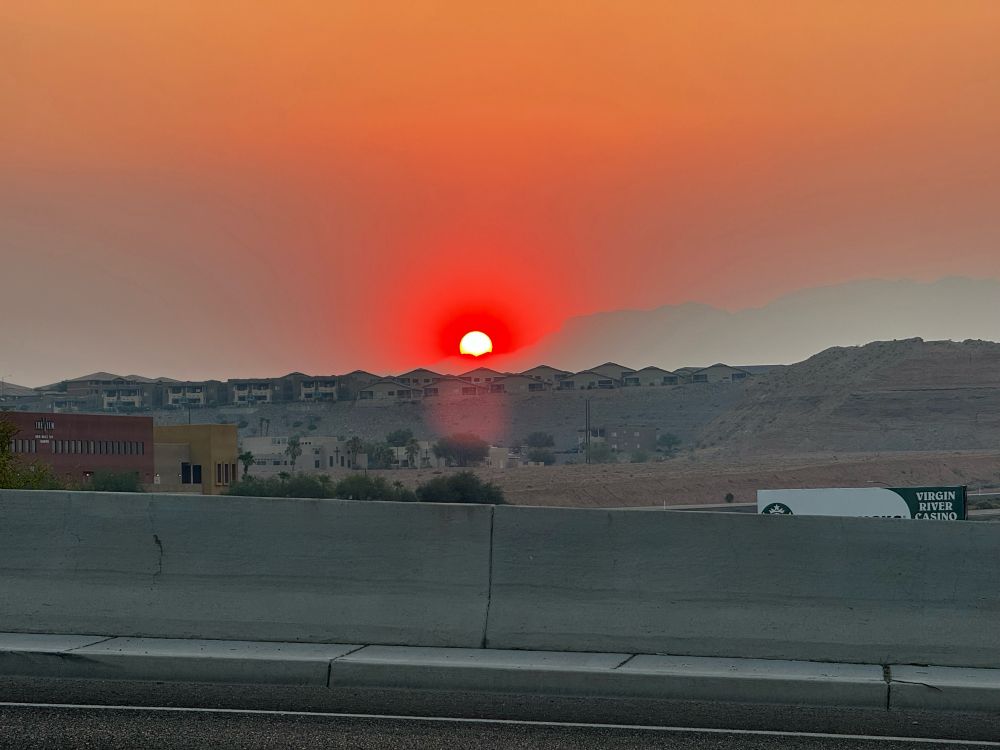 Smoky sunrise from behind a mountain over homes on a ridge top.