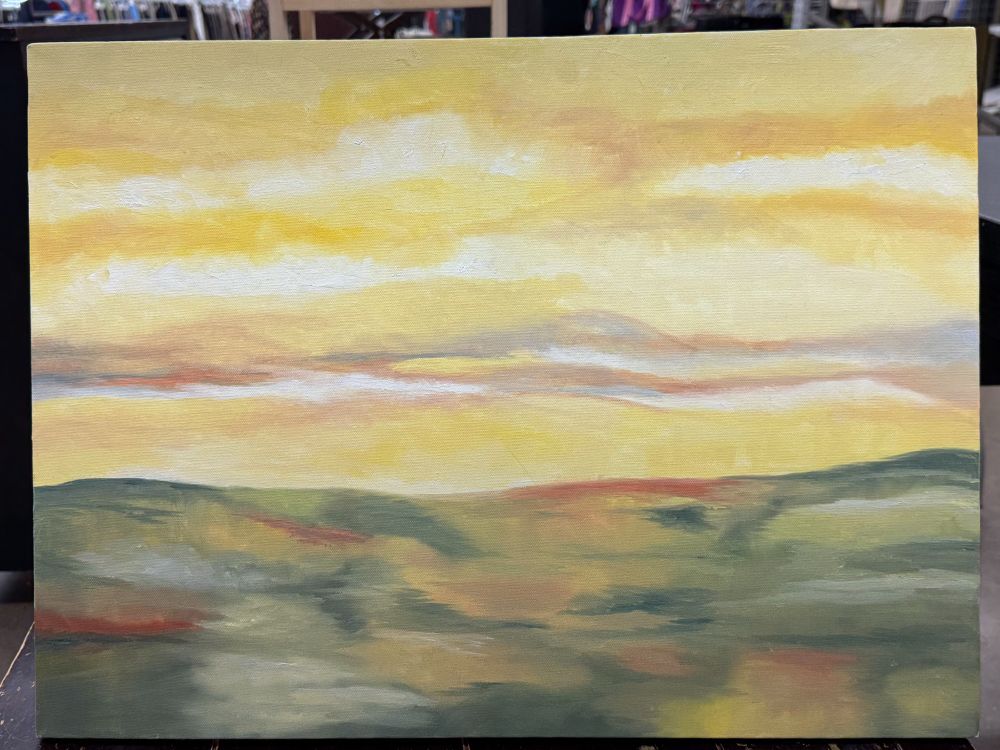 A color photograph of a thrift store painting depicting a bright, variegated, yellow cloudy sky above a mottled green, red, orange, and beige line of rolling hills. 