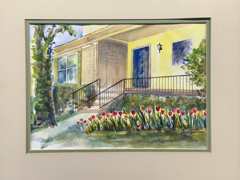 A thrift store painting at the Far West Goodwill, Austin TX. The matted watercolor depicts a shaded front porch with a yellow wall, fronted by a bed of blooming red tulips. Signed “Ann Sullivan.”