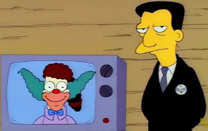An unlabeled screenshot from season 4 episode of The Simpsons, Kamp Krusty. The camp director glowers at the camera, while standing next to a televised introduction from Krusty the Clown (absent from the camp bearing his name). Krusty's introduction has the camp director's name badly dubbed over, resulting in a nasally "Mr. Black" when mentioned.
