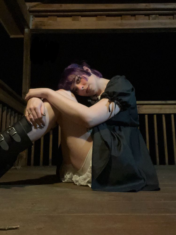 a picture of bunni sitting with their knees pulled up to their chest. they are resting their head on their knees and are looking at the camera 
