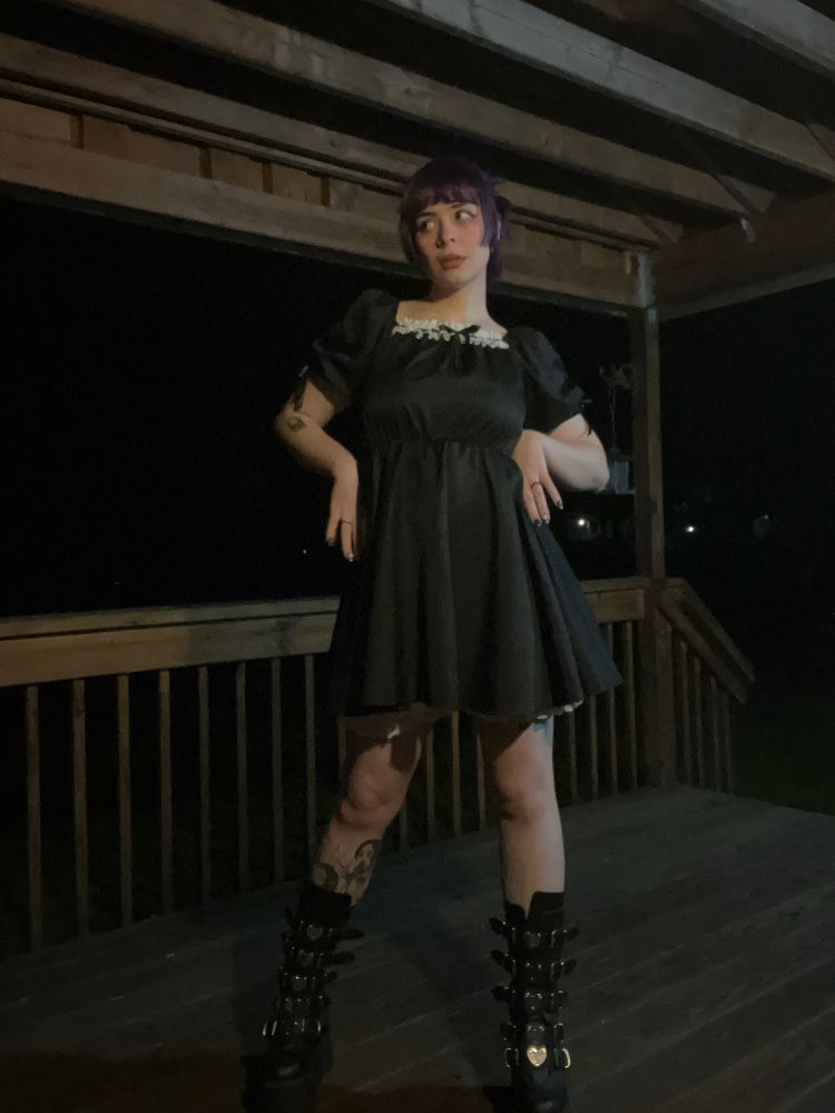 a full body picture of bunni in their platform demonia boots and a black dress. they have their hands on their hips and are looking off to the right 