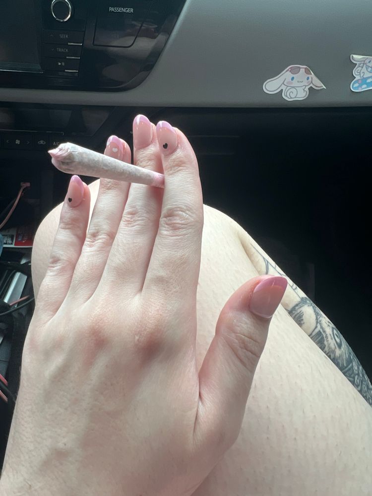 a picture of bunni’s hand holding a pink joint which matched their nails. they have round press ons with pink french tips and a small black heart