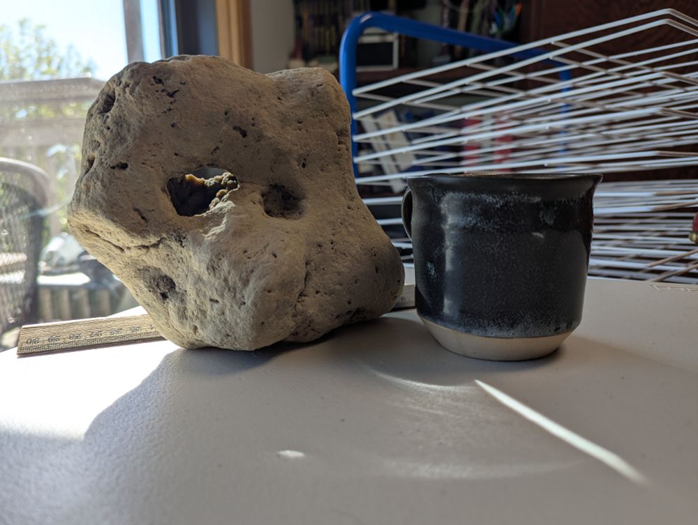 A large Hagstone next to a cup of coffee in front of a drying rack for prints