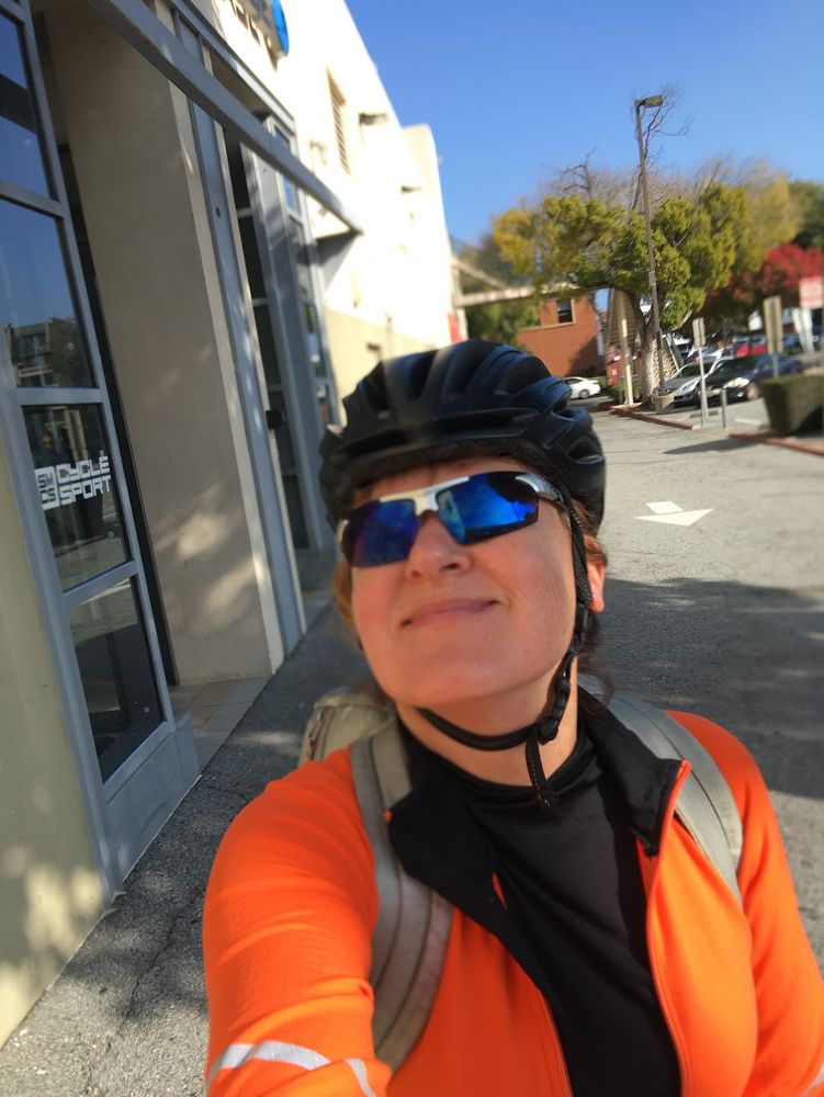 Erika Hall in an orange long sleeved bike jersey, black hemet, and douchebag cycling sunglasses looking optimistic about being able to find her way home. 