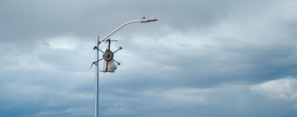 A drone and a bag of garbage hanging from a light pole against a cloudy sky. Screengrab from Pluribus.