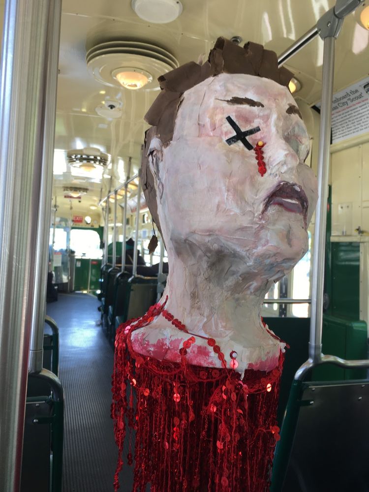 a paper maché head on a stick with festive red dripping sequins on the F train in san francisco