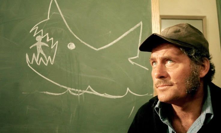 A cartoon shark eating a tiny person chalkboard sketch in a still from Jaws. Captain Quint is in the right of the frame with an I'll catch that shark for ten thousand dollars look on his face. 