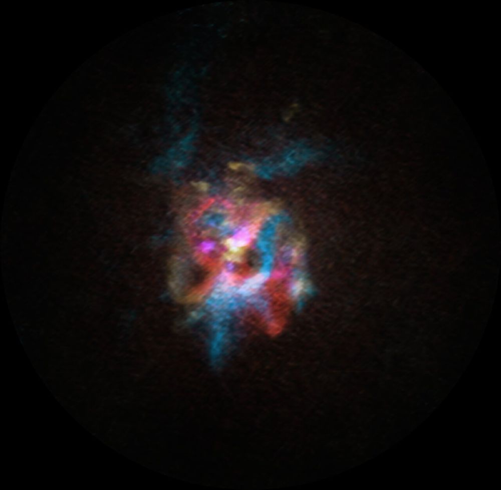 A fuzzy ball of gas and dust, with sections overlapping of red and blue. The background is completely black. In the centre towards the top of the cloud is a lighter patch of whitish red.