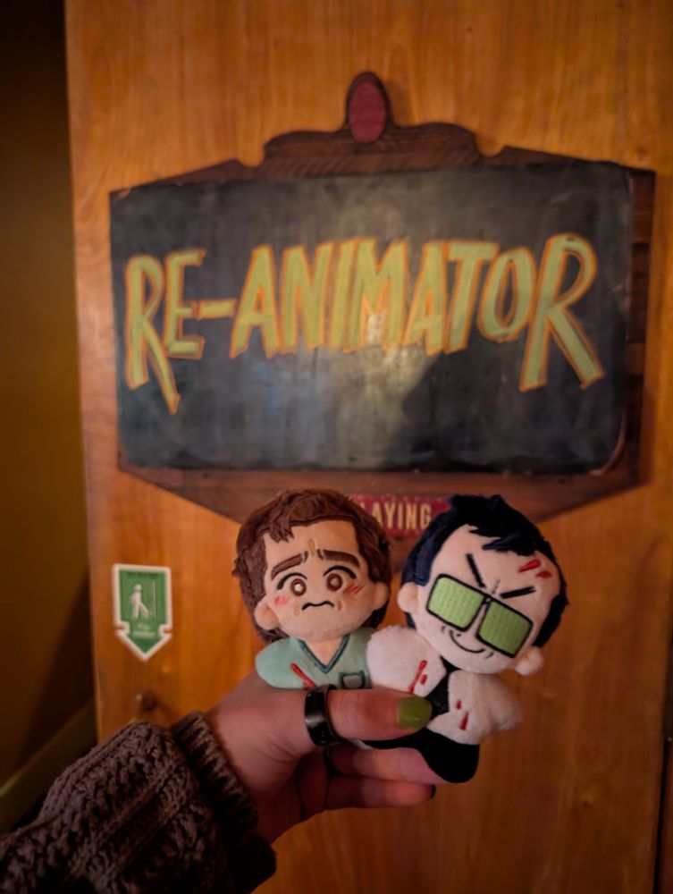 Dan and Herbert plushies being held beneath a hand-drawn sign that reads "Re-Animator"
