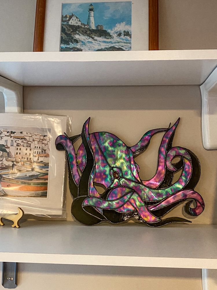 Iridescent stained glass octopus on a shelf with some nautical prints 