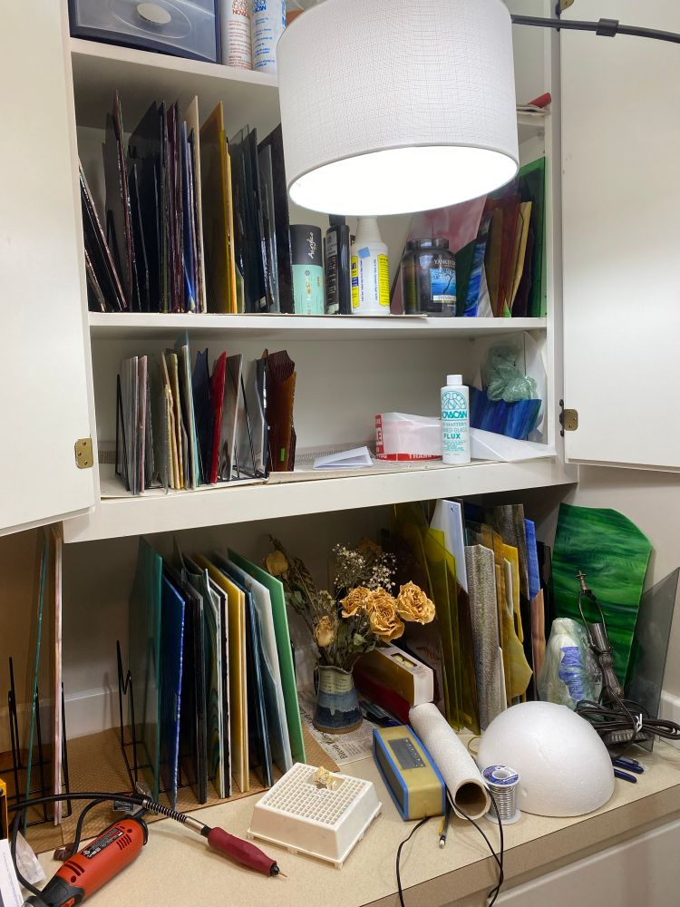 A cupboard full of glass and other supplies over a counter also holding glass and various supplies 