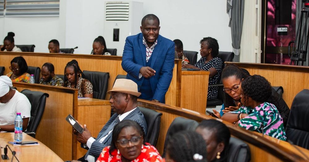 Attendees at a formal meeting inside a conference room, Senior Lecturer Precious Adade Duodu is  standing and addressing others who are seated and listening attentively.
