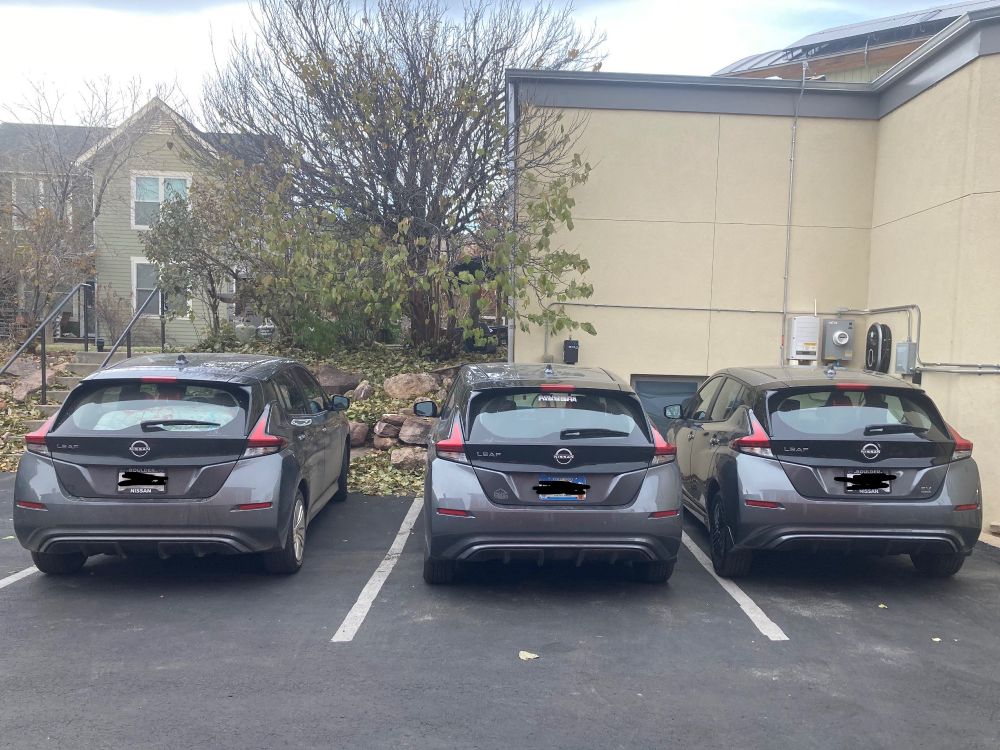 A row of three dark grey Nissan Leaf EVs in a small parking lot.