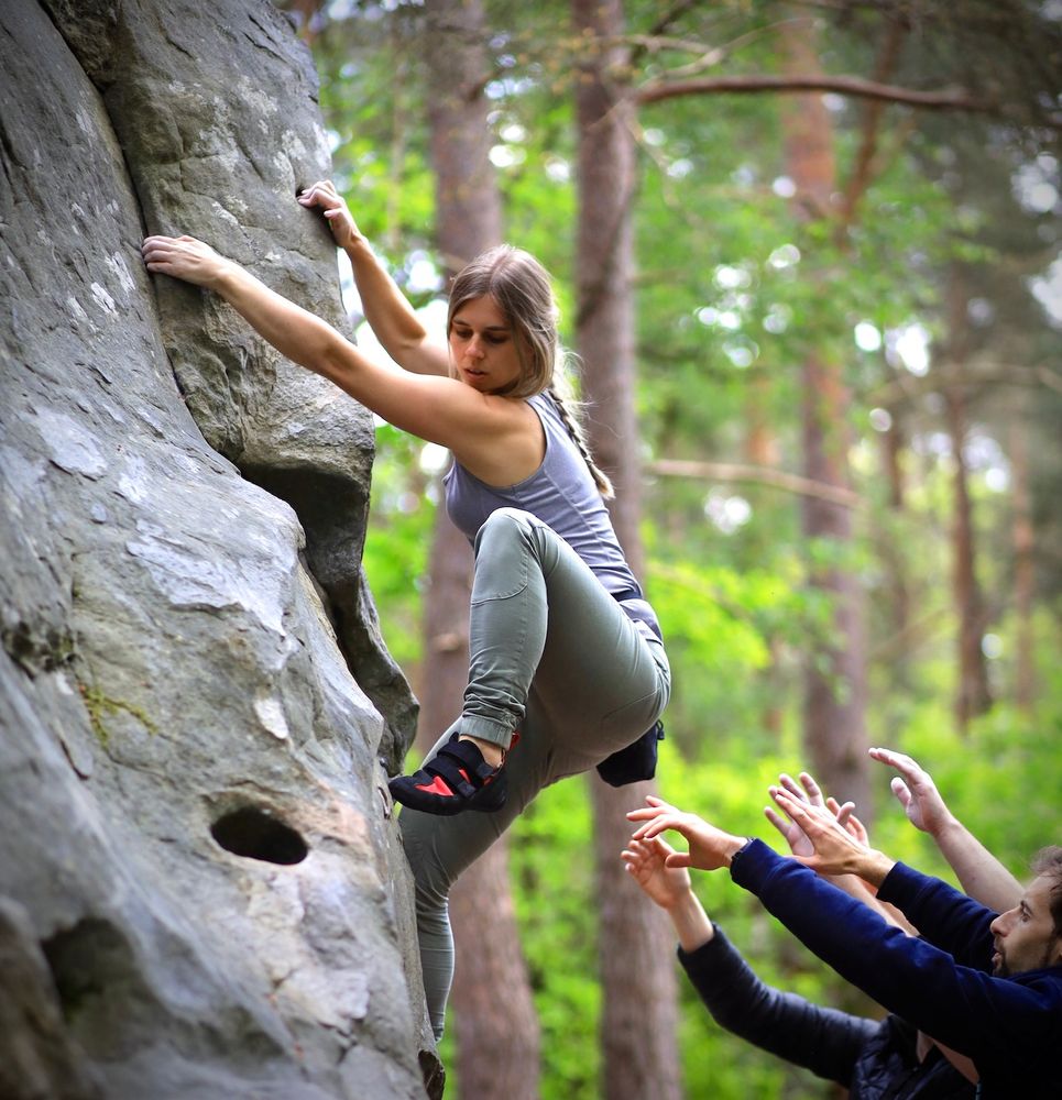 Emma climbing a boulder in the forests of Fontainebleau with three people spotting.