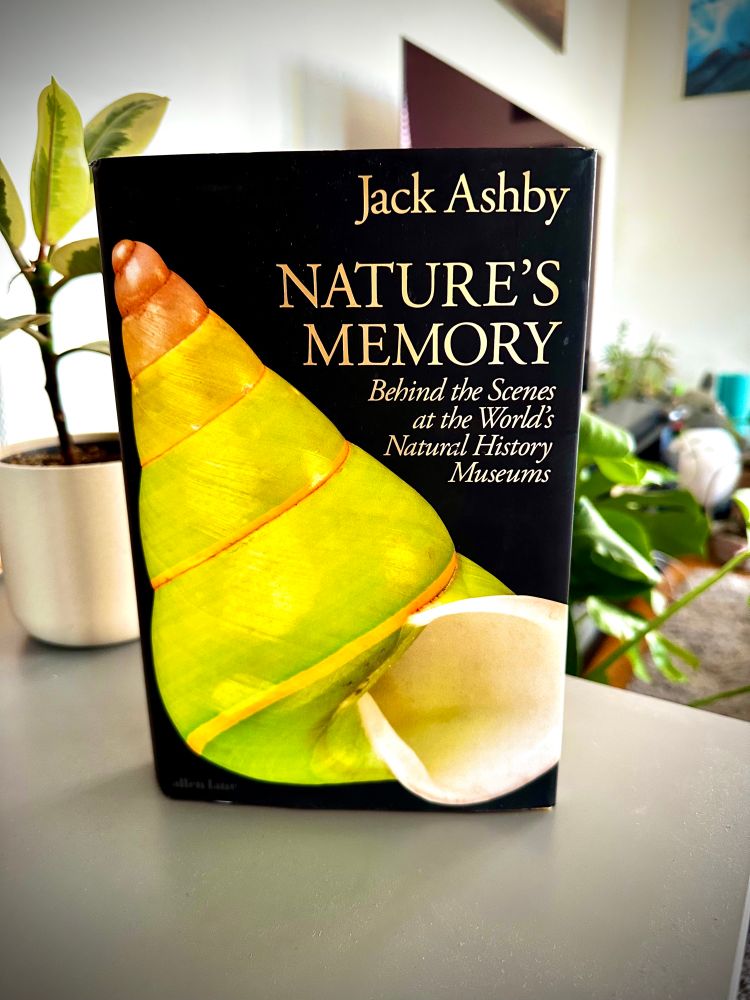 The front cover of the book by Jack Ashby, titled ‘Nature’s Memory: Behind the scenes at the word’s natural history museums’. On the front cover is a green shell.