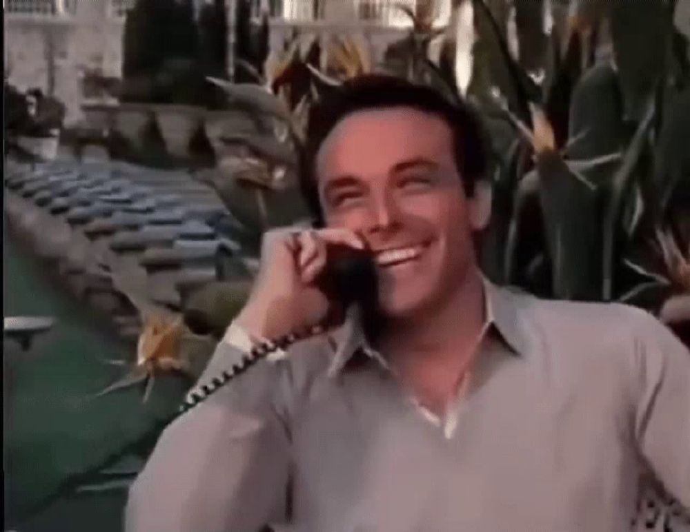 a man is smiling while talking on a phone in front of a pool .