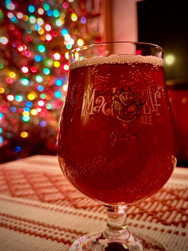 A glass of two-year-aged Mad Elf beer with a lot Christmas tree in the deep background 