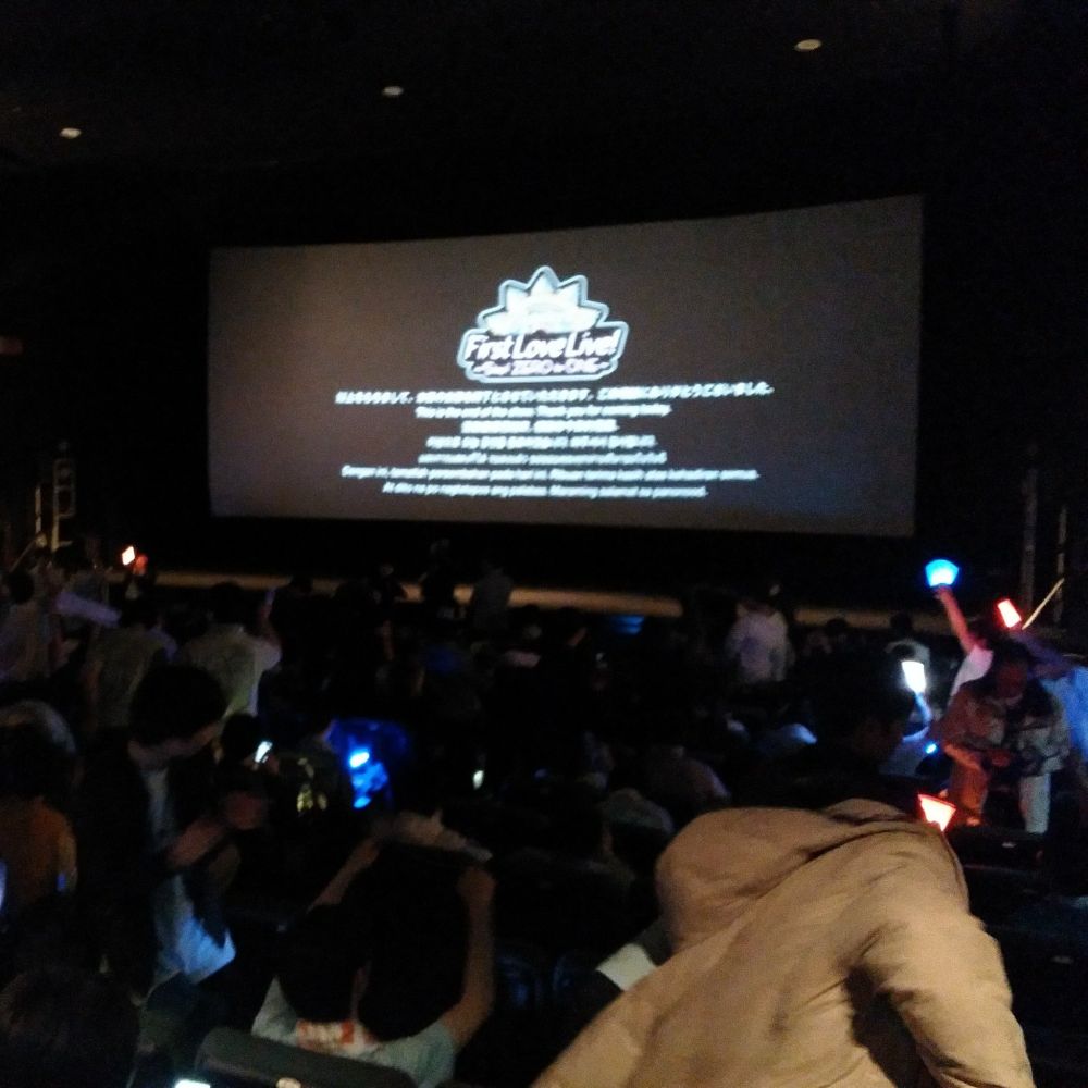 photo from a cinema screening of Aqours First Live at Shinjuku Wald9, February 2017. people in the rows in front are waving penlights in different colours. 
