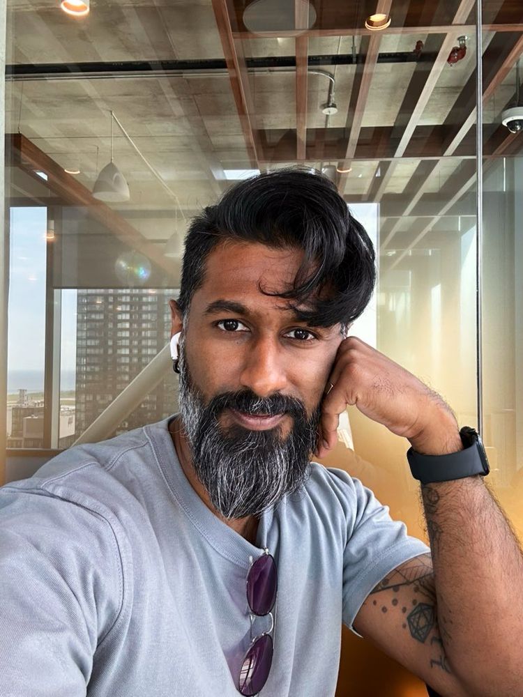 Marino, selfie, grey blue tshirt, tinted glasses hanging off of shirt, grey beard.