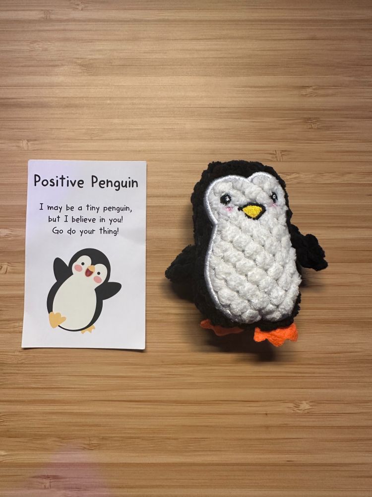 Left: A note on white paper card saying: Positive Penguin
I may be a tiny penguin, but I believe in you! Go do you thing! 

Right: A black/white penguin plushie

Backround: Woodgrain desk
