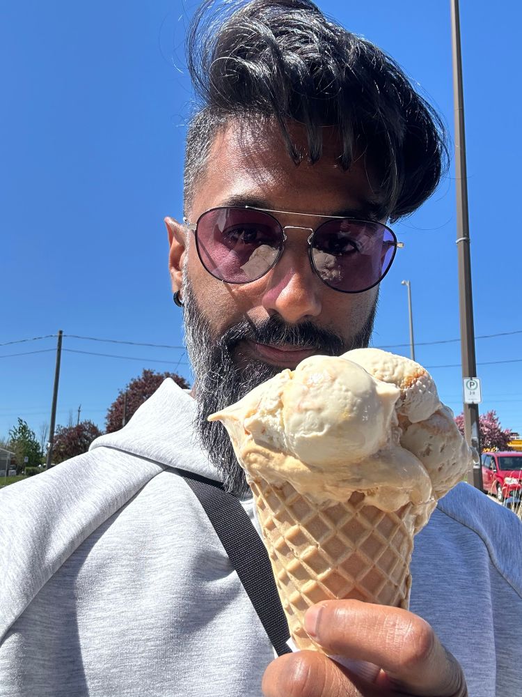 Marino selfie in red/purple glasses, sunny blue skies,  holding a huge waffle cone with several different scoops (pralines and cream + salty caramel toffee)