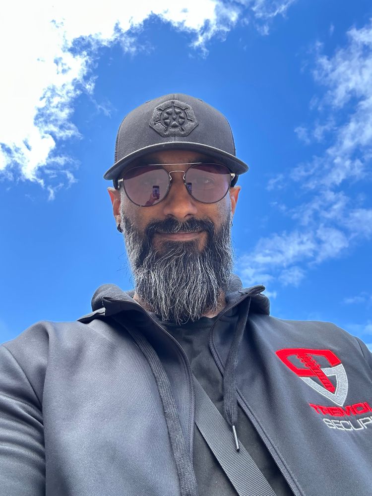 Marino with a black Kubernetes logo on black hat wearing a black hoodie with the tremolo logo and a blue sky with clouds