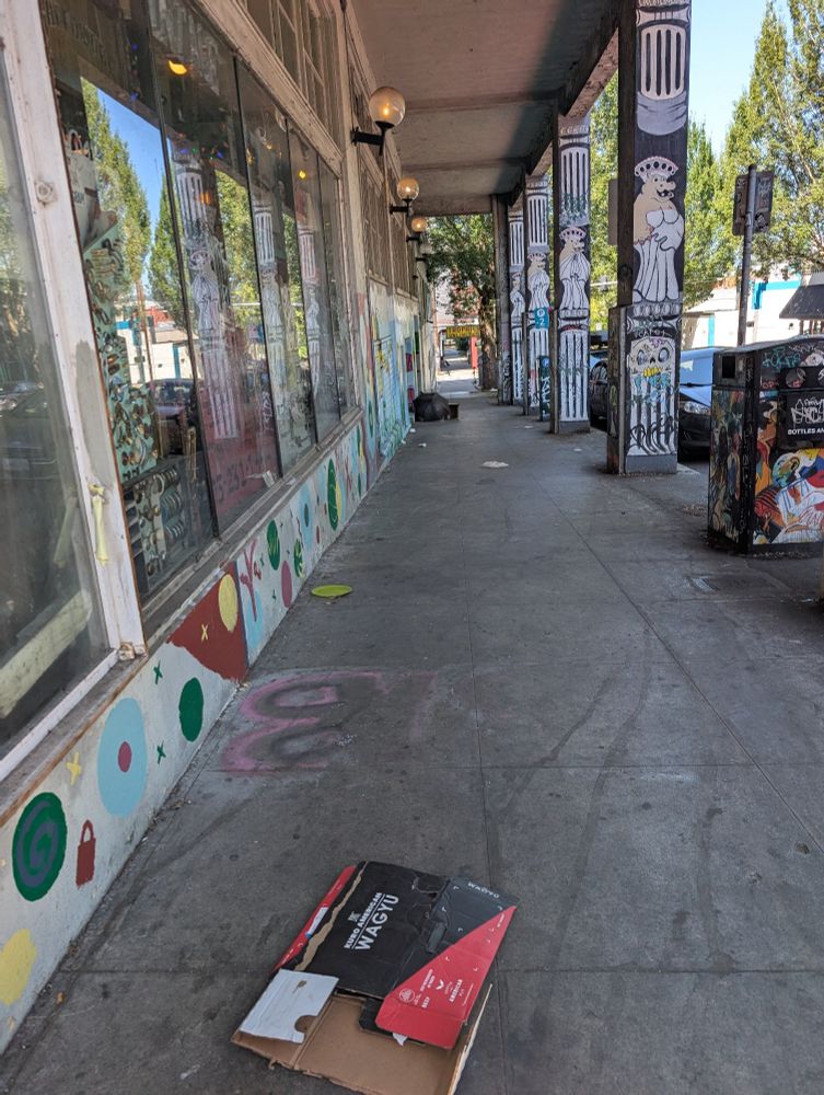  In the foreground a box from a wagyu beef, undoubtedly from one of Portland's best restaurants which is just down the street. In the background an umbrella obscures a woman sleeping on the sidewalk. 