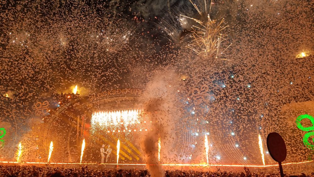 Foto der Abschlusszeremonie des Festivals, vor der Euphoria Stage. Zwei tanzende Licht-Figuren auf der Bühne. Sehr viel Effekte mit Nebel, Konfetti, Laser, Feuer und Feuerwerk im Bild.