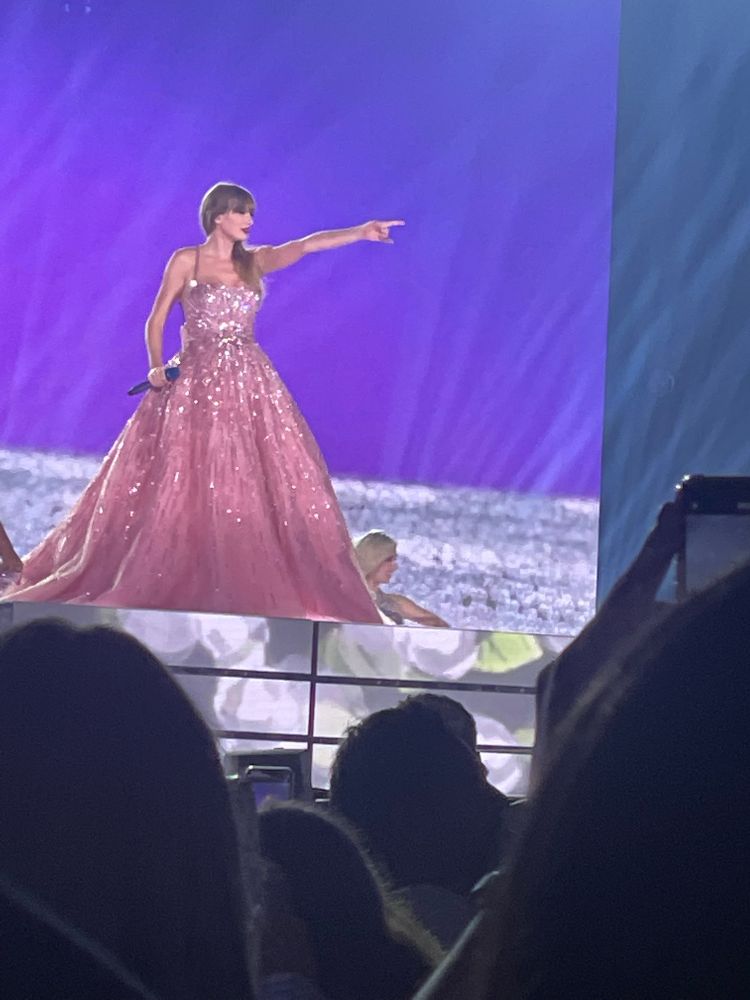 taylor swift wearing a pink sparkly gown and performing enchanted at the eras tour. she’s looking out at the crowd and pointing. 