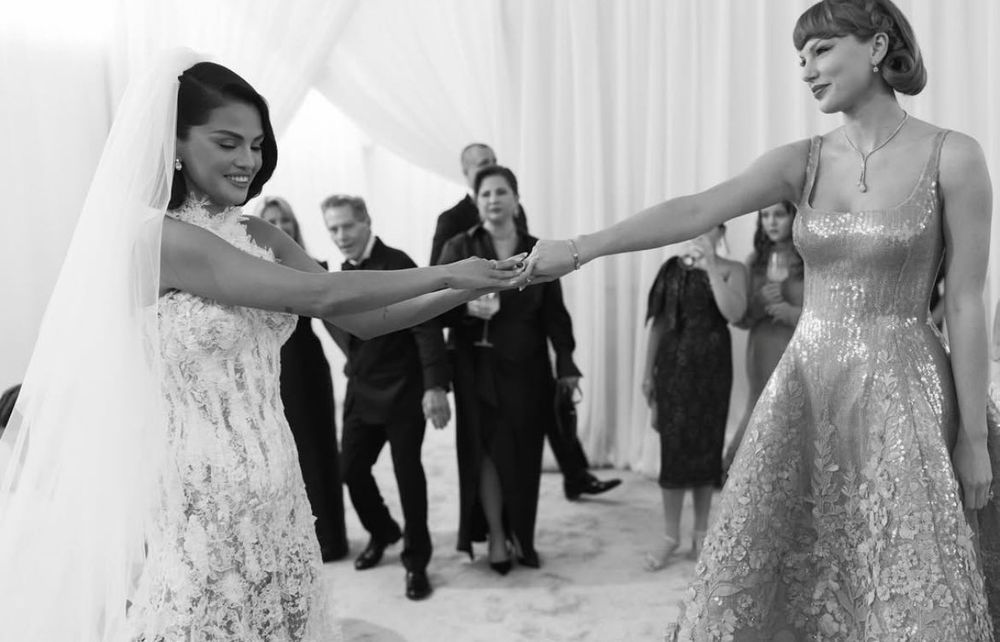 black and white photo of selena gomez and taylor swift. selena is wearing a lace sleeveless wedding dress with a veil. taylor is wearing a sleeveless long dress with sequins. men in suits are in the background. 