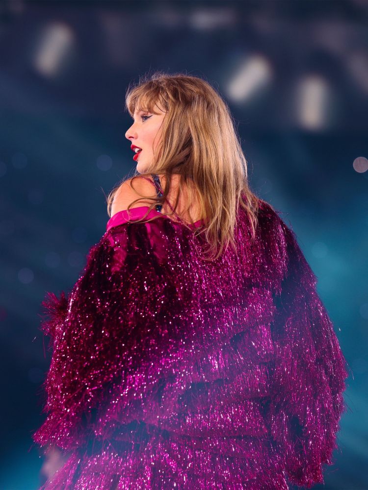 Taylor Swift wearing a magenta sparkly jacket, looking over her shoulder, closing night of the eras tour