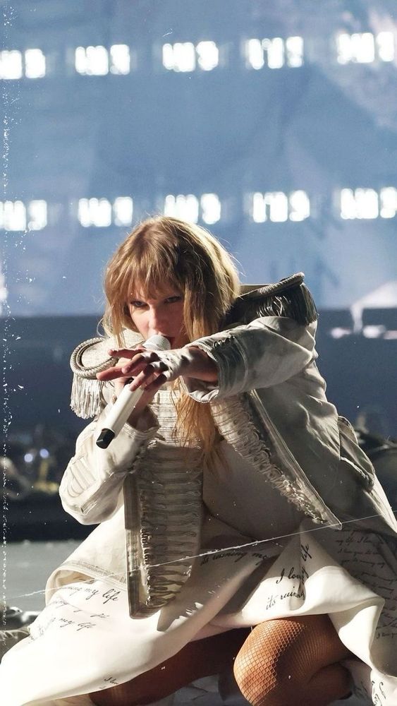 taylor swift performing the smallest man who ever lived at the eras tour. she’s kneeling and wearing a white dress and jacket. 
