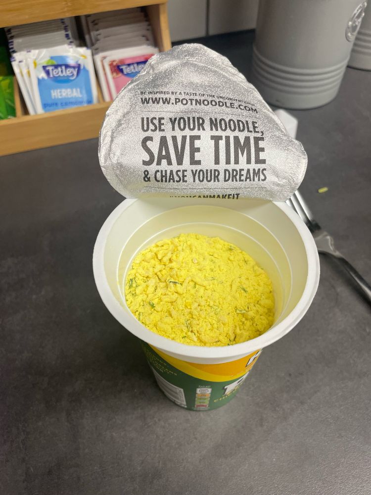 An opened Pot Noodle brand instant ramen cup. The inside of the foil lid is printed with “Use Your Noodle, SAVE TIME & Chase Your Dreams”. I make less than minimum wage. 
