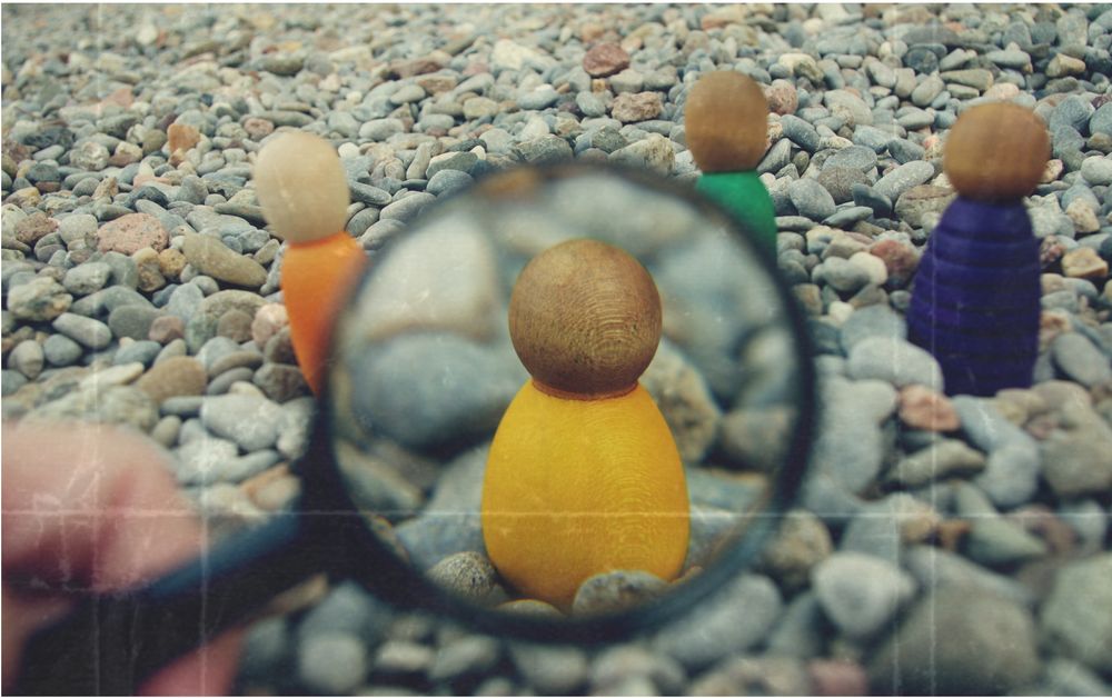En la imagen se observa una figura de madera de la marca Grapat, vestida de amarillo, enfocada a través de una lupa sobre un suelo de piedras. A su alrededor, se ven otras figuras desenfocadas en segundo plano.

La escena transmite la idea de poner el foco en un individuo concreto, simbolizando atención, observación o valoración particular dentro de un grupo. Puede interpretarse como una metáfora de la mirada cuidadosa hacia la infancia o la importancia de reconocer la singularidad de cada persona.