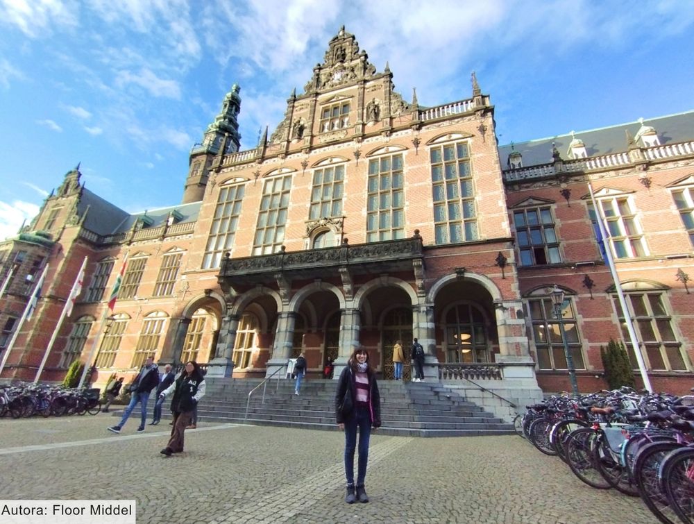 Imagen de la doctoranda, Rosa Sitjes, frente a la sede principal de la Universidad de Groningen. El edificio destaca por su fachada de ladrillo rojo y su elegancia.
Aunque se trata de una ciudad donde llueve con frecuencia, en la fotografía el cielo aparece despejado, con algunas nubes que no anuncian lluvia. El edificio está intensamente iluminado por el sol.
La autora de la imagen es Floor Middel.