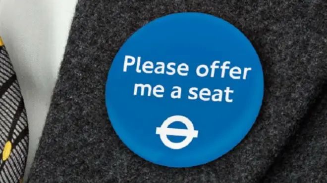 Badge on a grey lapel, white text and TfL rondel on a blue background: Please offer me a seat 