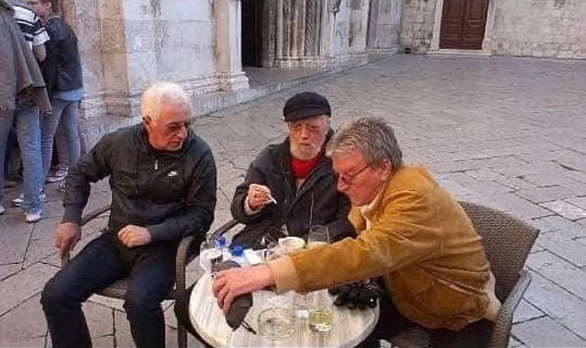 Three old men at a cafe table outside a cathedral. It is very Jugoslavian.