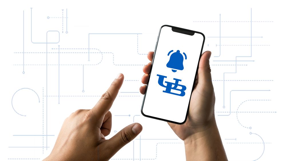A hand holding a smartphone with a UB logo on it. 