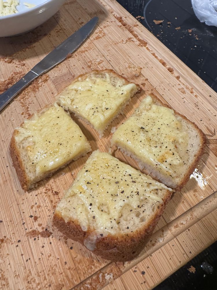 Slice of lightly peppered melted cheese on bread cut into four.