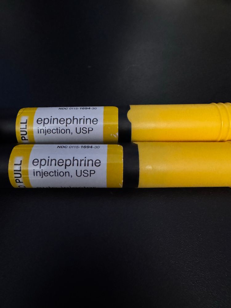 Two ADRENACLICK epinephrine injectors in their cases on a black background