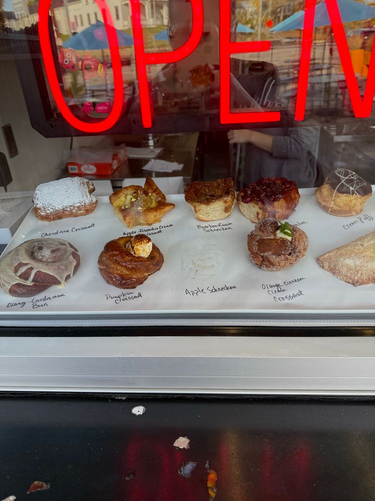 Various pastries laid out on white parchment paper under a red neon sign that says OPEN.