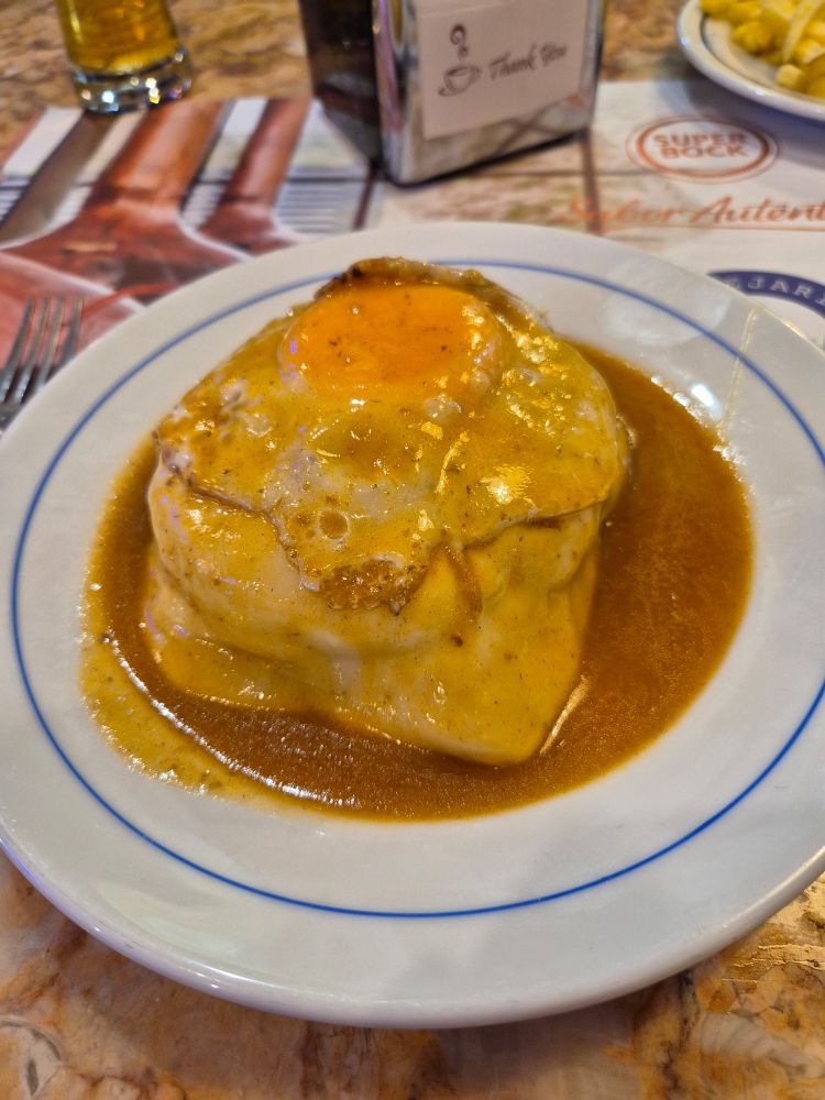 A francesinha - ham, steak and cheese in a sandwich with a fried egg on top with a beer and tomato sauce