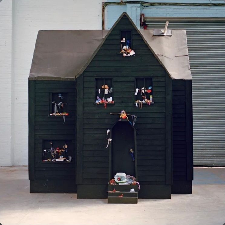 A black wooden house with trash on the windows in front of a warehouse door
