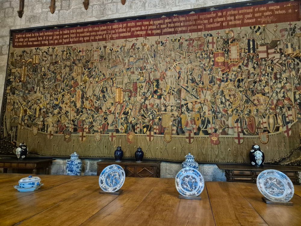 A tapestry that spans a wall with blue and white porcelain plates on a table in front 