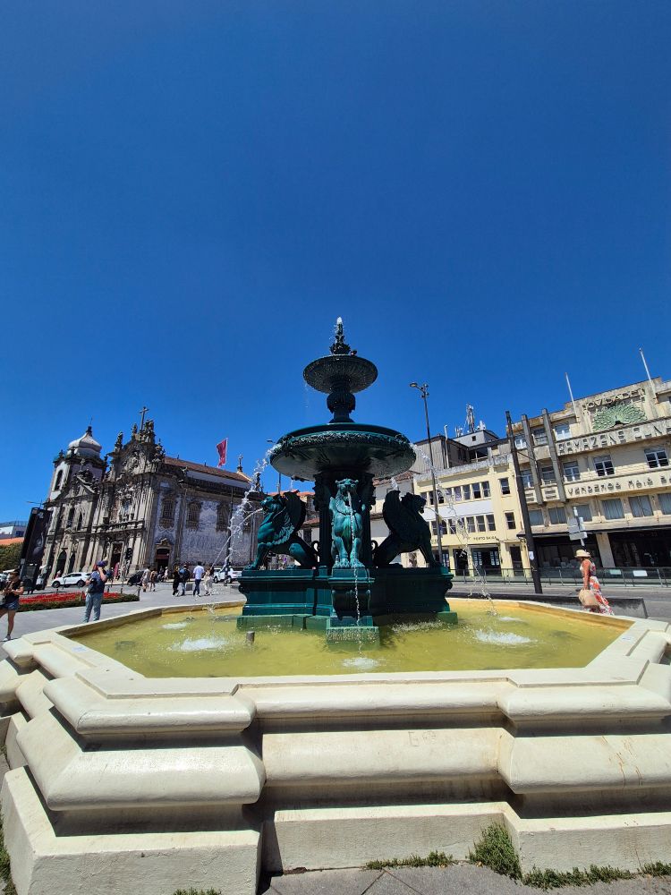 A green metalwork fountain with a church in the background 