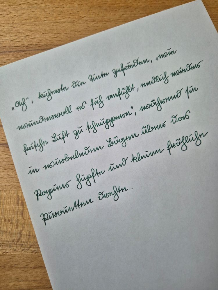 Auf einem weißen Blatt Papier steht mit grüner Tinte:
„Ach“, kicherte die Tinte zufrieden, „wie wundervoll es sich anfühlt, endlich wieder frische Luft zu schnuppern“, während sie in wirbelnden Bögen über das Papier hüpfte und kleine fröhliche Pirouetten drehte.