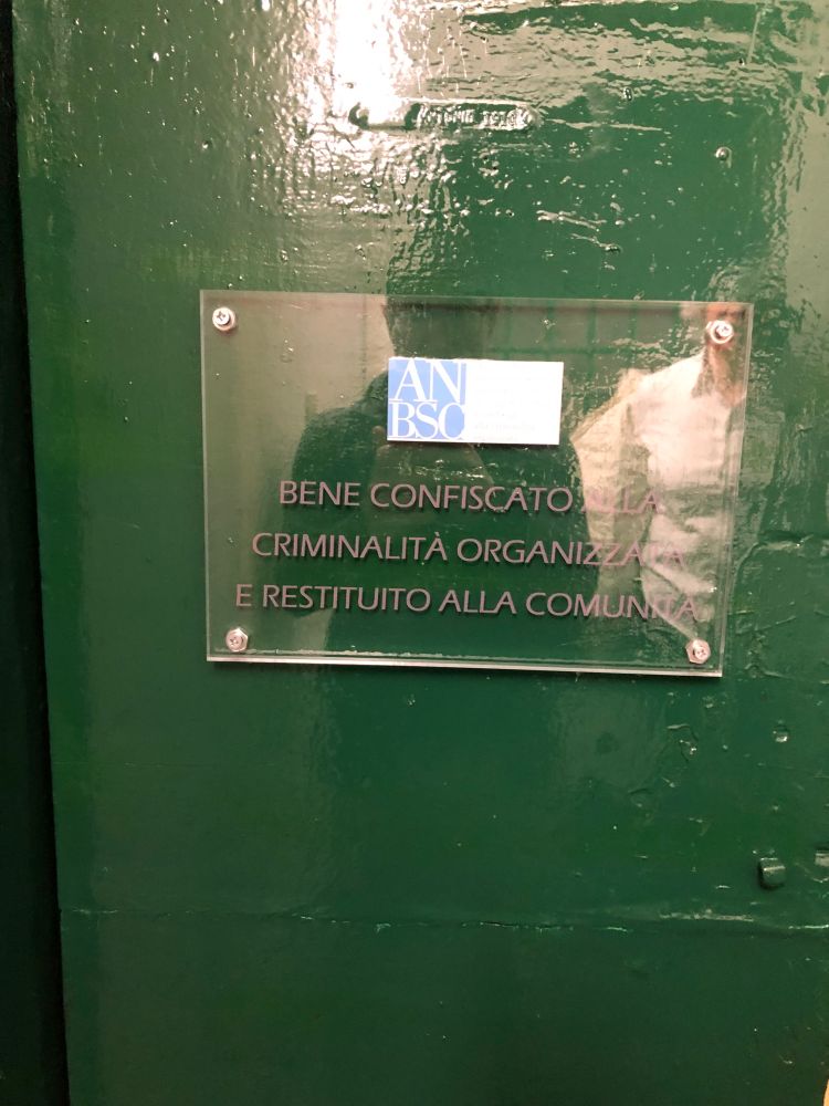 Plaque fixée à l'entrée d'un immeuble pour indiquer que le bien a été confisqué à la mafia et restitué à la commune pour un usage social