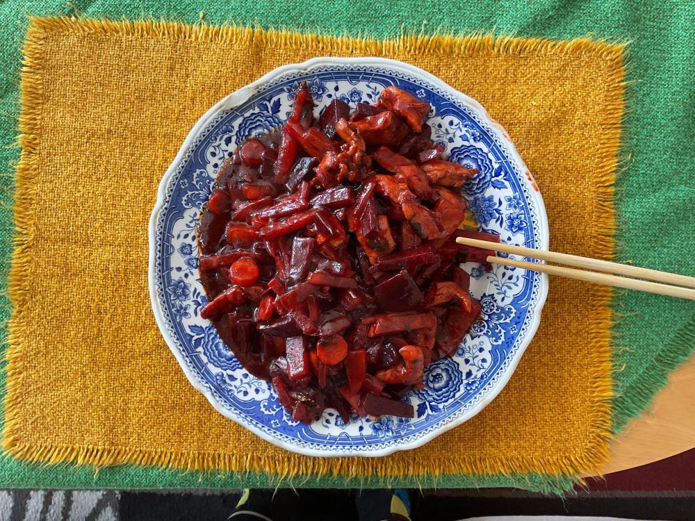 Blick von oben auf einen Teller, Motiv Burgenland blau. Darauf kleingeschnittenes Gemüse und Fleisch, alles rot. Am Tellerrand zwei Essstäbchen. Unter dem Teller ein gelbes Tischset, darunter die grüne Tischdecke aus dem gleichen Stoff. 