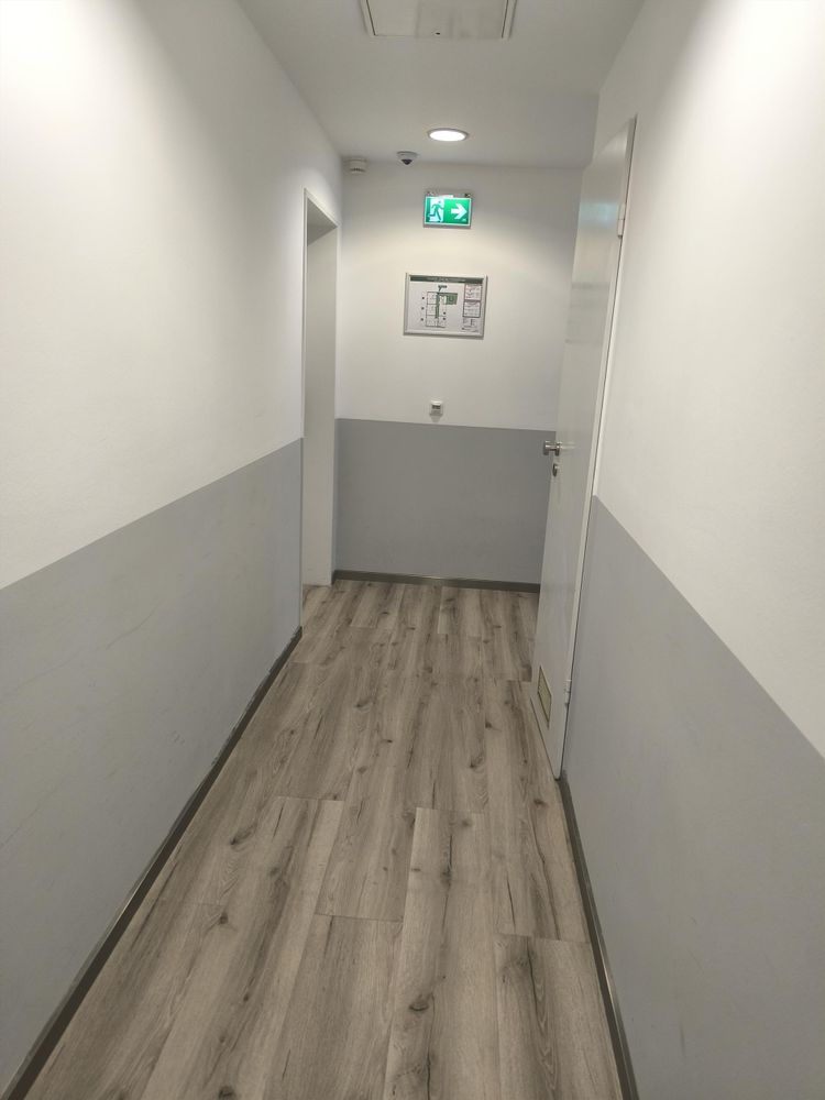 Leerer Hotelflur mit braunem Laminat und weißen Wänden. Leider nicht sehr einladend. 